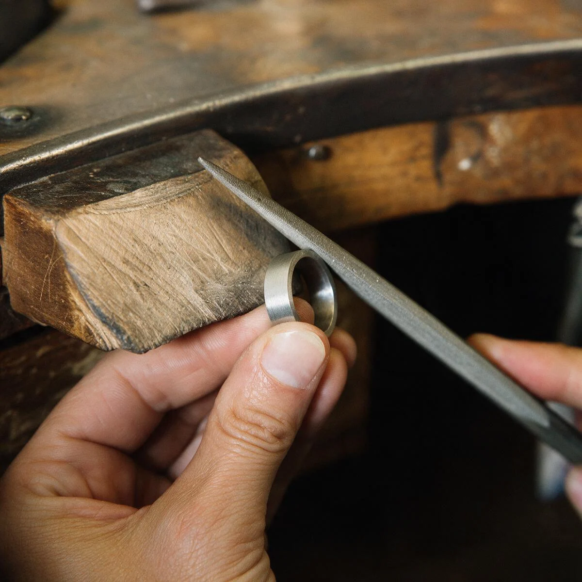 Jeweller hand-filing a steel wedding band at the bench in the Barcelona workshop